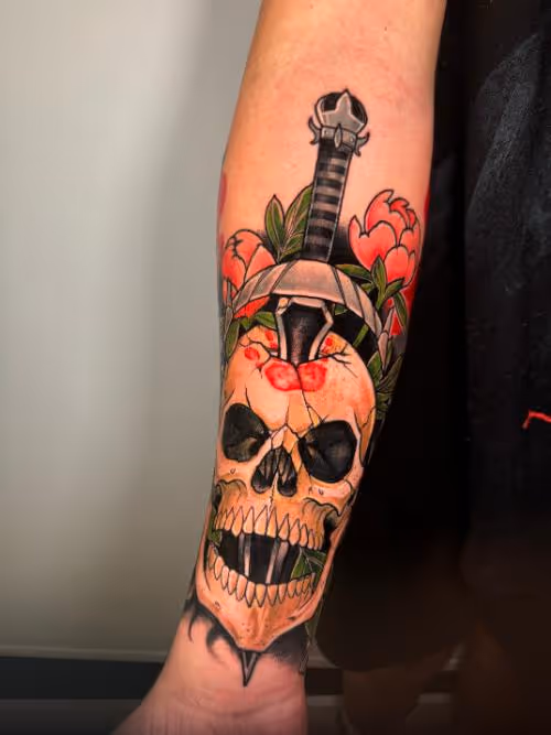 Forearm tattoo of a skull pierced by a dagger, with red flowers and green leaves