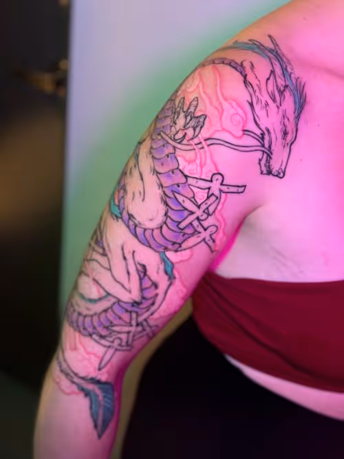 Dragon and swords tattoo wrapping around upper arm under pink and green lighting.