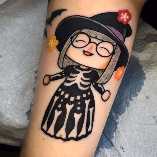 Smiling cartoon witch in skeleton dress tattoo with hat, flowers, and a small bat