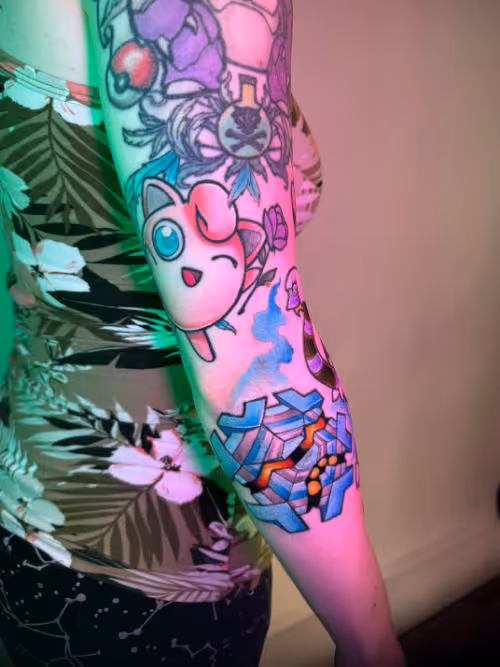 Arm with colorful tattoos, including a Jigglypuff tattoo under pink and green lighting