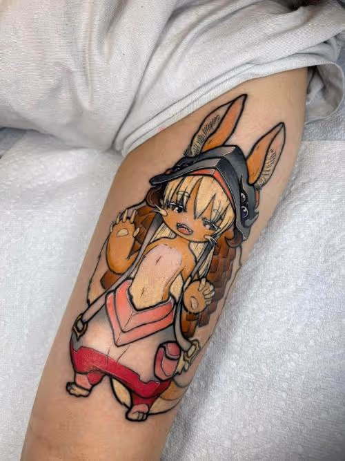 Anime-style chibi bunny-eared character tattoo with helmet and pink outfit on a forearm.