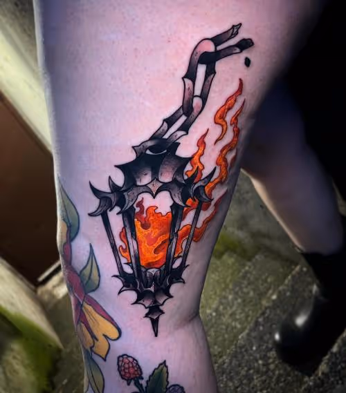 Black lantern tattoo with orange flames on a thigh.