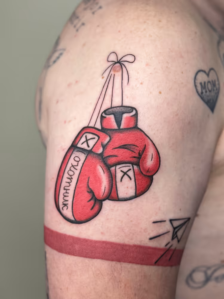 Red boxing gloves tattoo hanging by laces on an upper arm