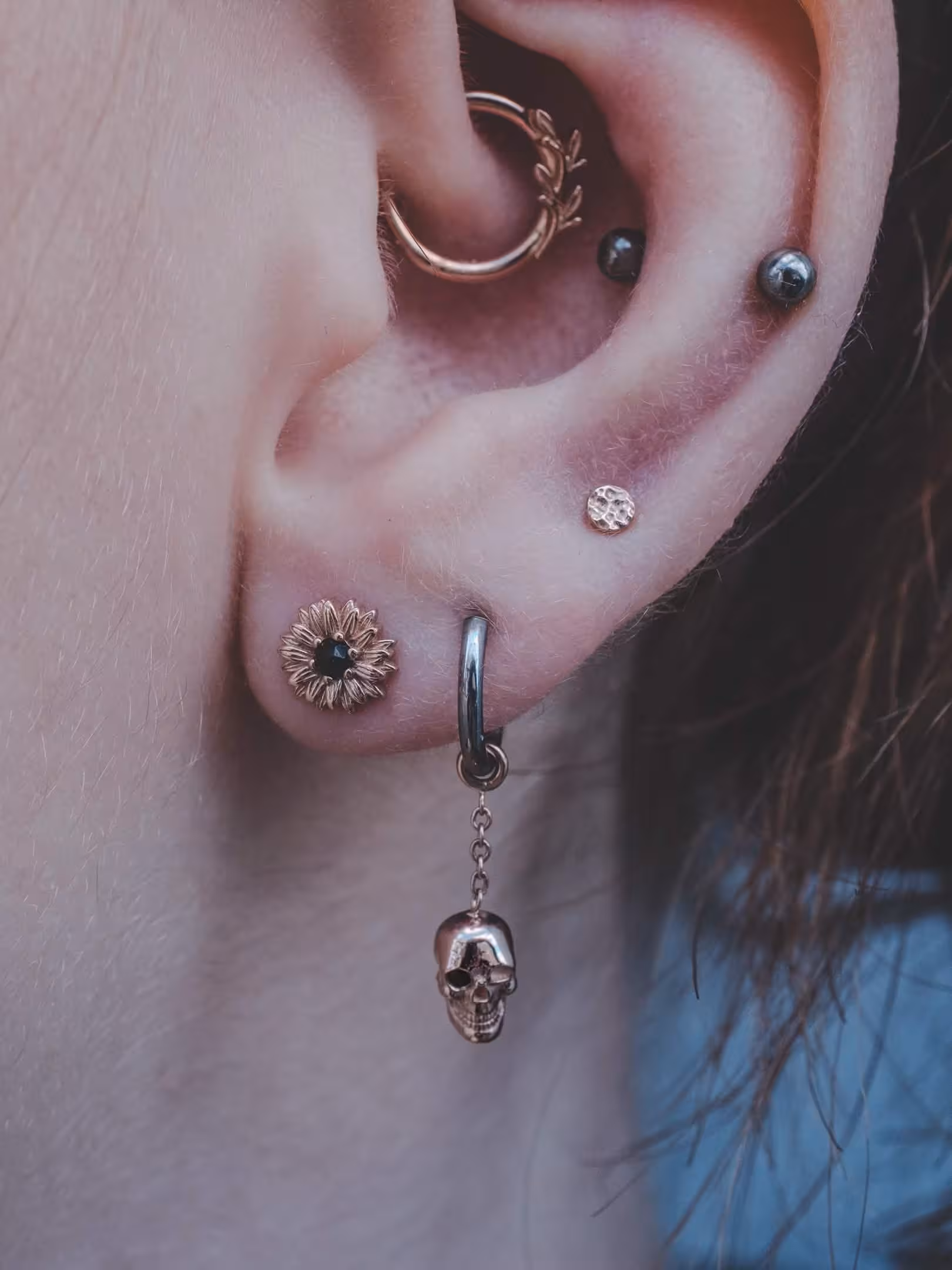 Multiple ear piercings with laurel hoop, two cartilage studs, floral stud, and skull dangle.