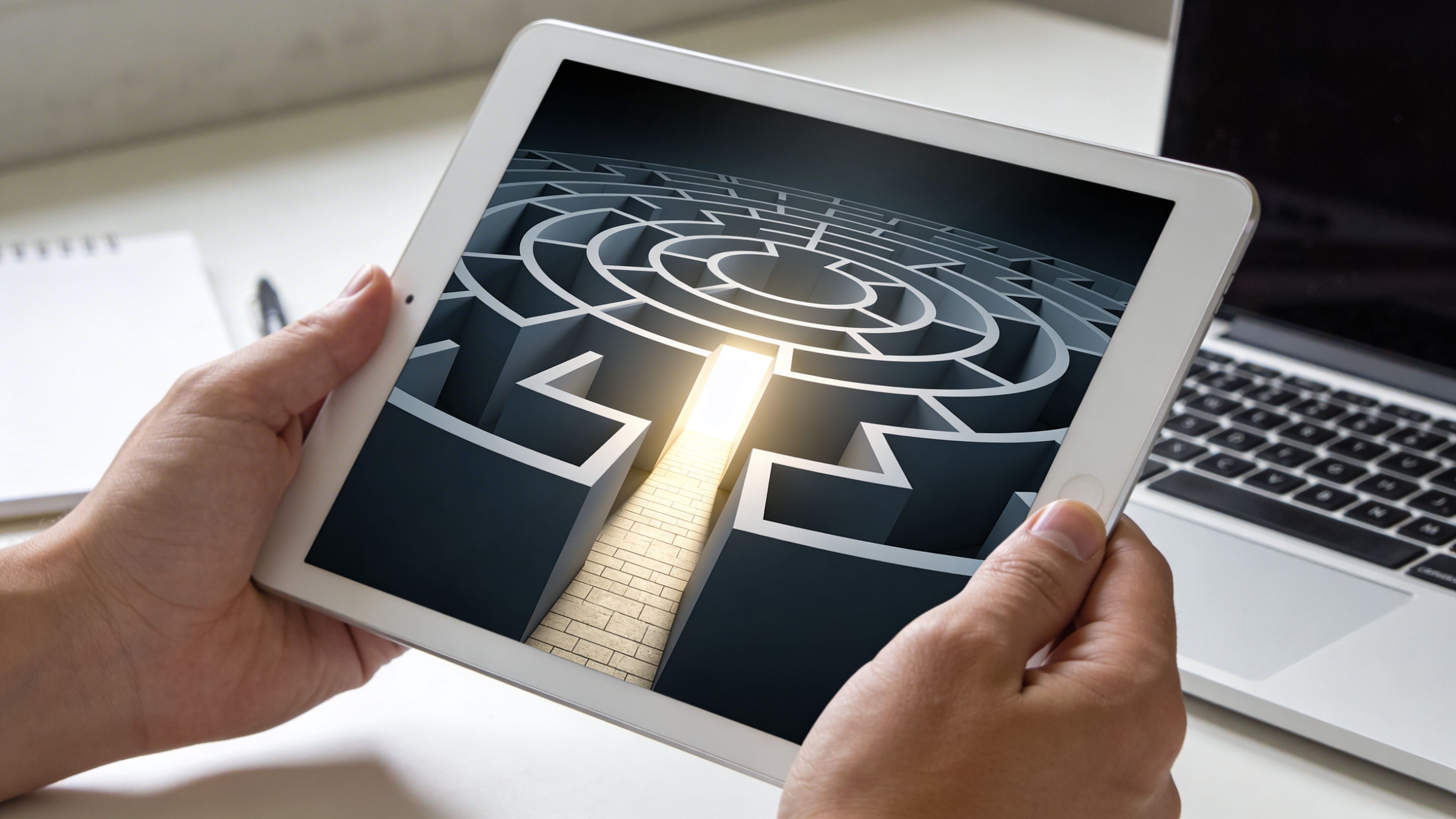 Persona sosteniendo una tableta con la imagen de un laberinto y una salida iluminada en pantalla.