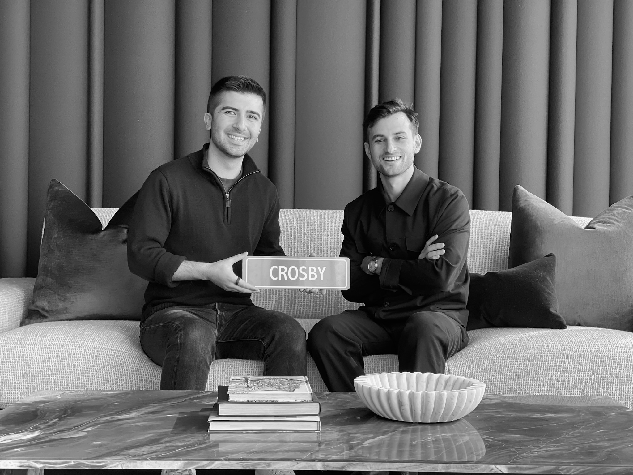 John and Ryan, founders of Crosby, sitting on a couch holding a plaque that says ‘Crosby’