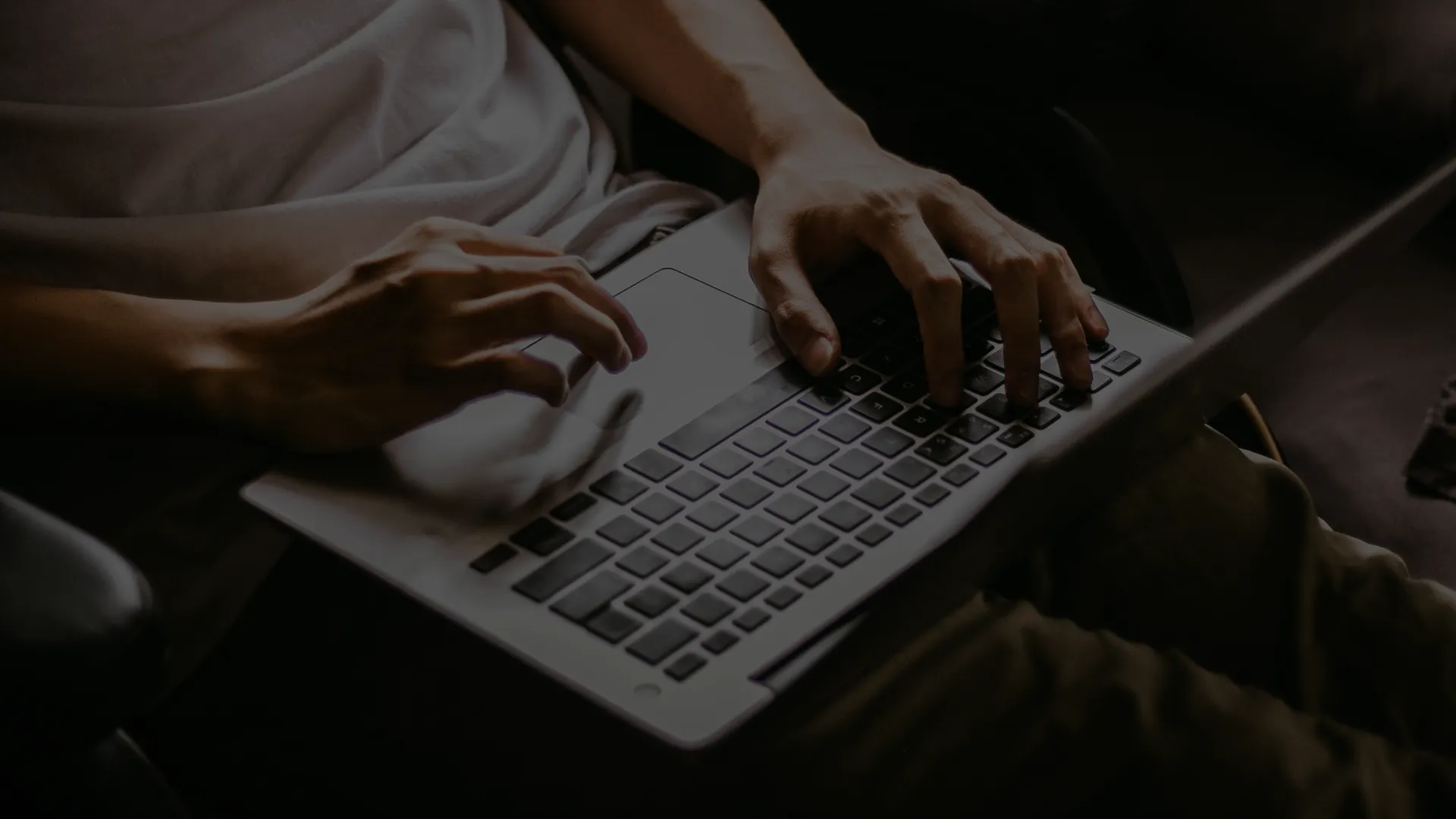 Person typing on a laptop keyboard in a dimly lit setting.