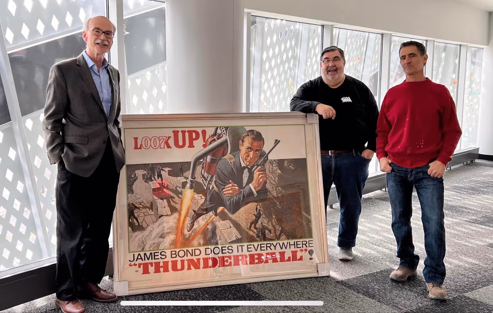 Men holding a large James Bond poster and smiling