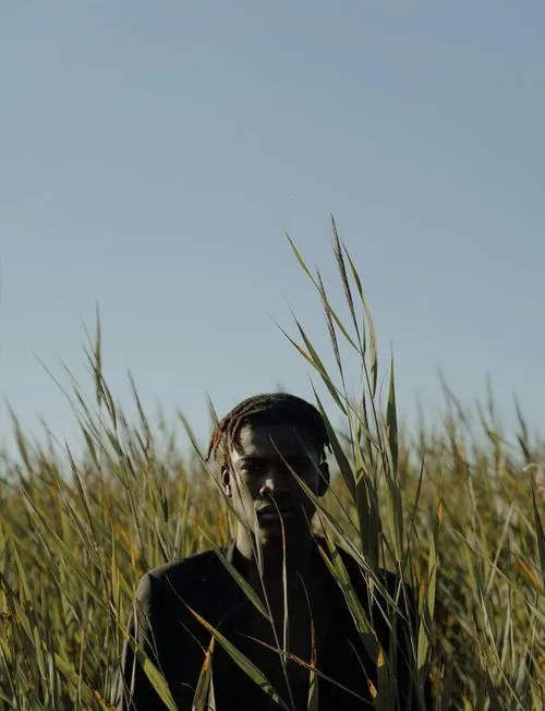A man stands amidst tall grass, surrounded by nature, embodying tranquility and connection to the outdoors.
