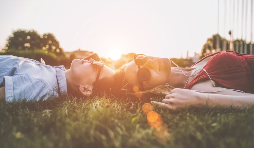 A man and woman laying on grass with the sunlight setting in the background