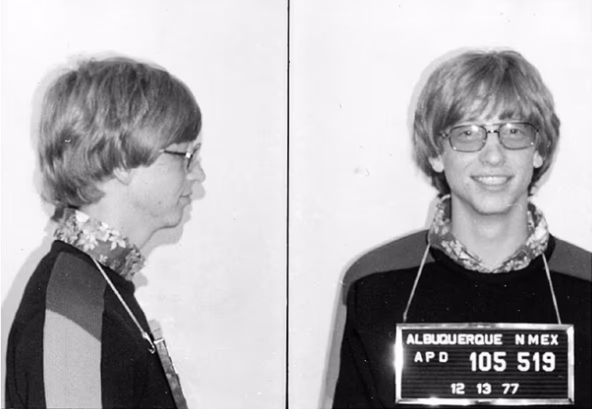 Black and white mugshot showing a young man with glasses and a light-colored collared shirt, taken from two angles: profile and frontal. A badge with "ALBUQUERQUE NMEX" is visible, dated December 13, 1977.