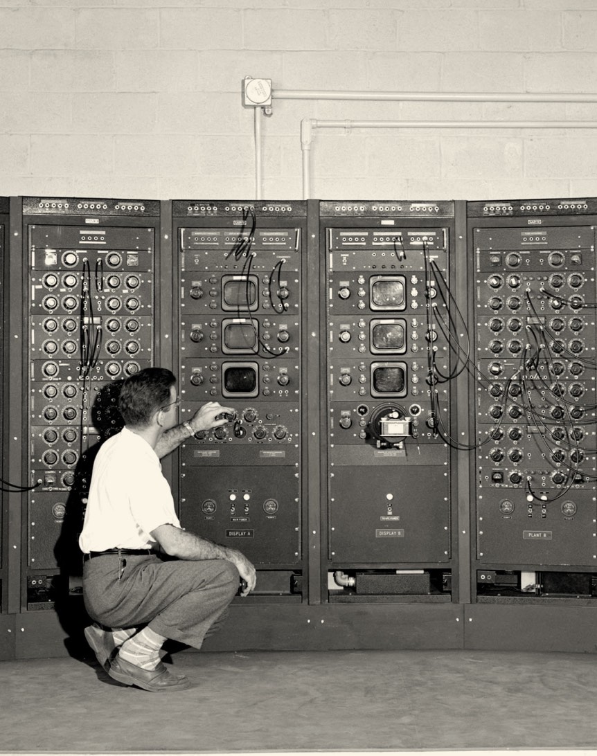 A technician adjusting controls on a large vintage electronic equipment panel, featuring multiple dials and switches, in a workshop setting.