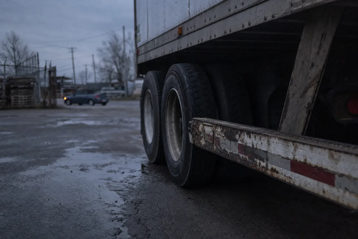 Rear wheels and underride guard of a parked semi trailer, passenger car behind for scale