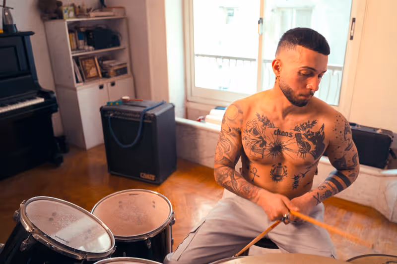 Photo of a shirtless tattooed guy wearing Designed by Ducky sweatpants and playing the drums
