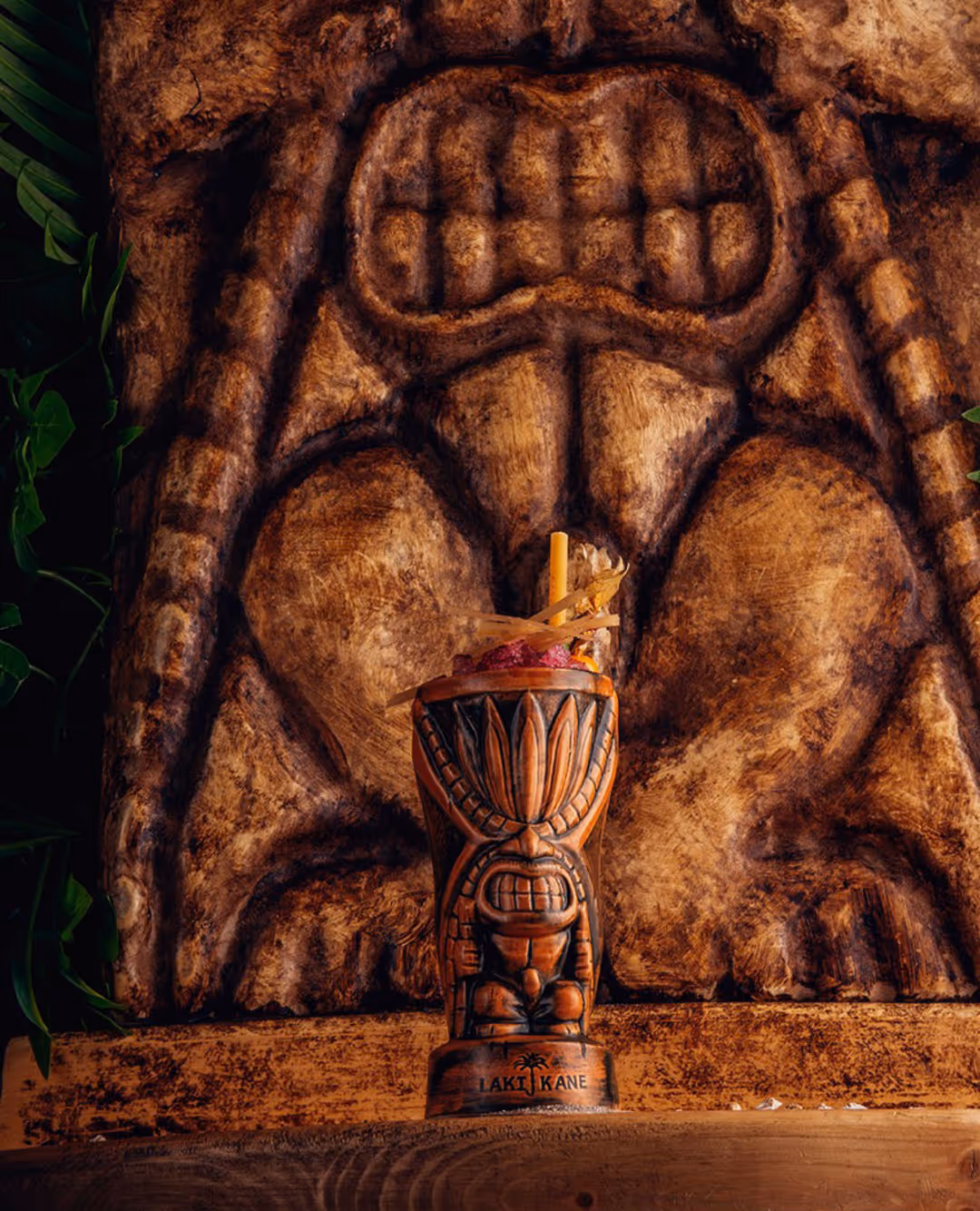 Photo of a Laki Kane cocktail in a wooden carved cup, with carved wooden statue behind it