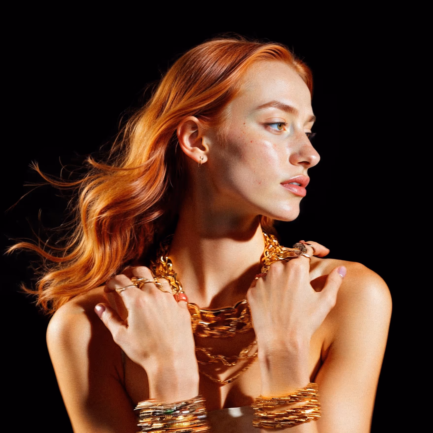 A portrait of a woman with flowing red hair, wearing layered gold jewellery, posed gracefully against a dark background. The image, used by an artificial intelligence agency, highlights modern creativity and elegance with a futuristic aesthetic.