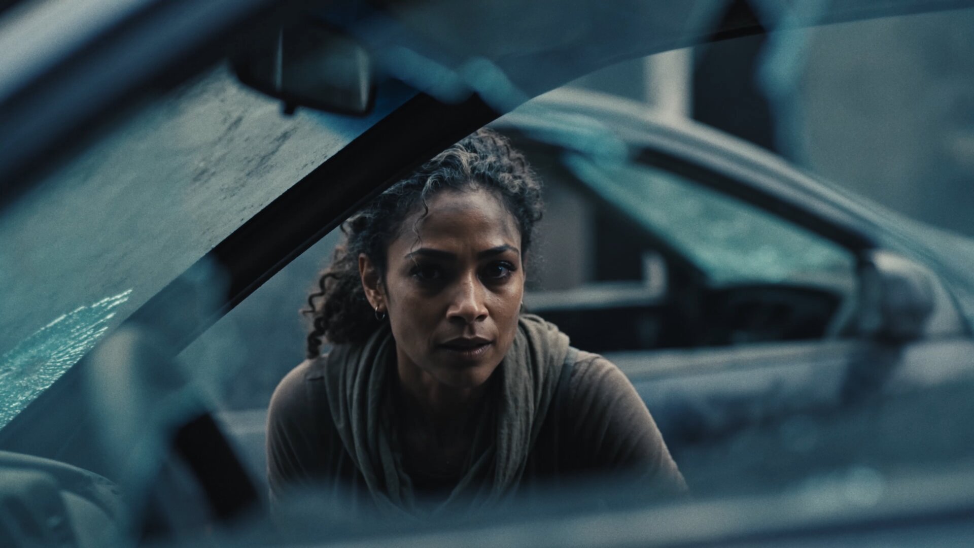 Trailer still, woman seen through a shattered car window