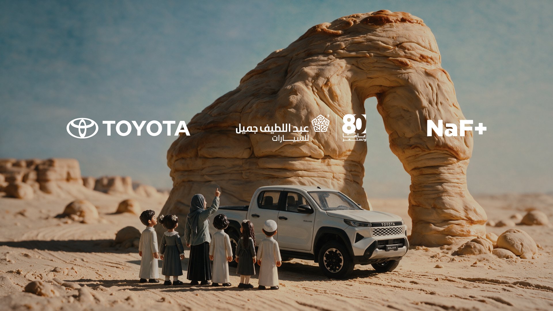 Clay family and a Toyota Hilux beneath a desert rock arch with Toyota, Abdul Latif Jameel and NaF+ logos