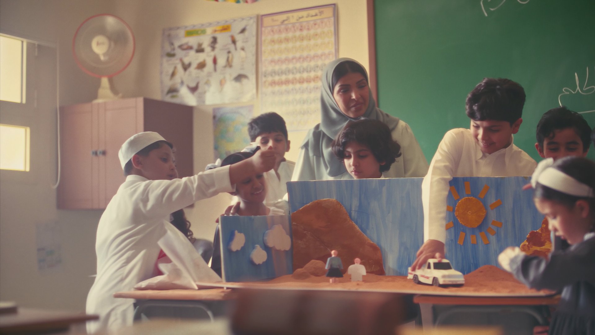 Students and teacher building a desert model with a toy car in class