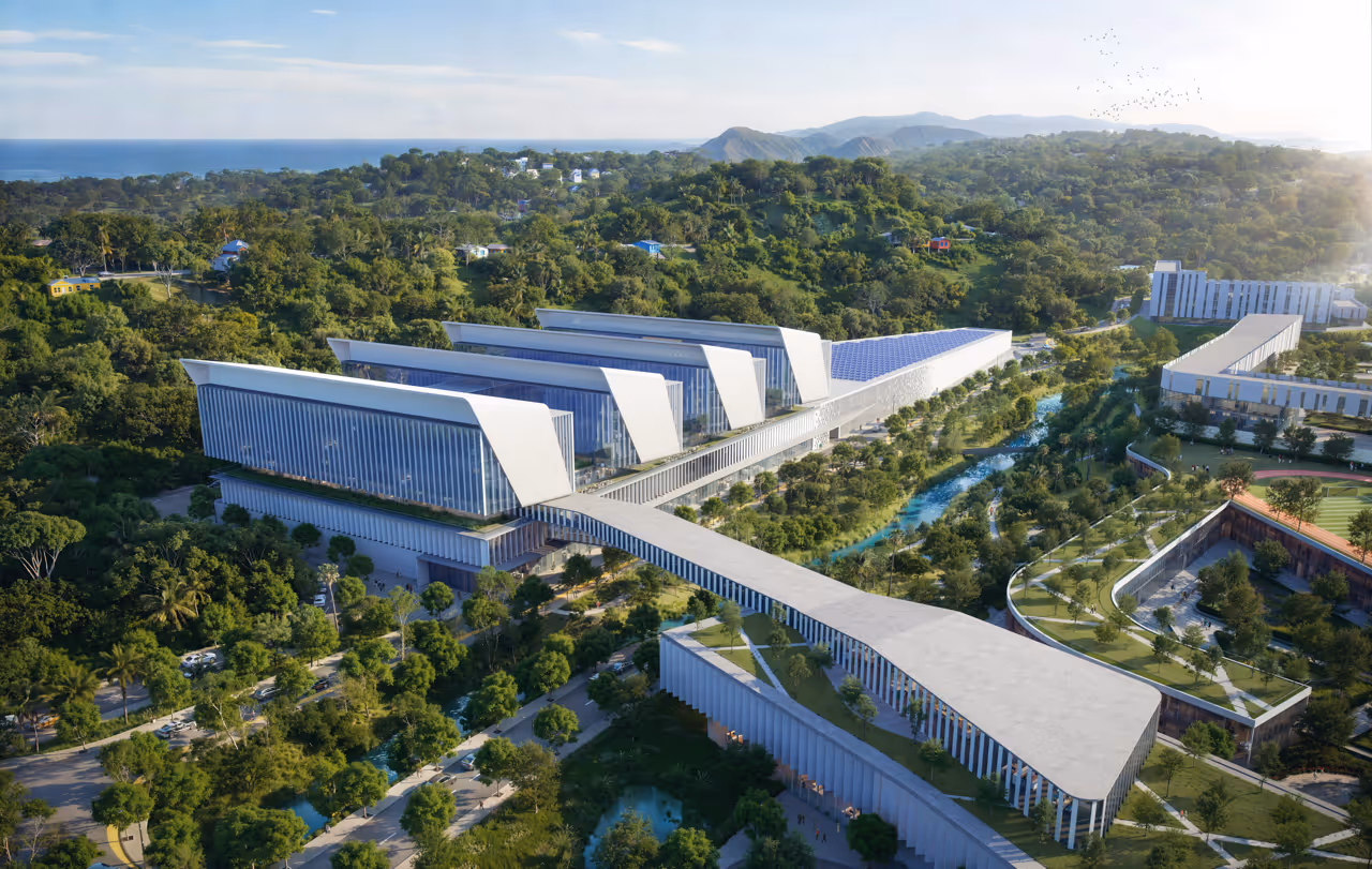 Aerial view of a large modern hospital complex surrounded by greenery, with solar panels on some rooftops and mountains in the distance.