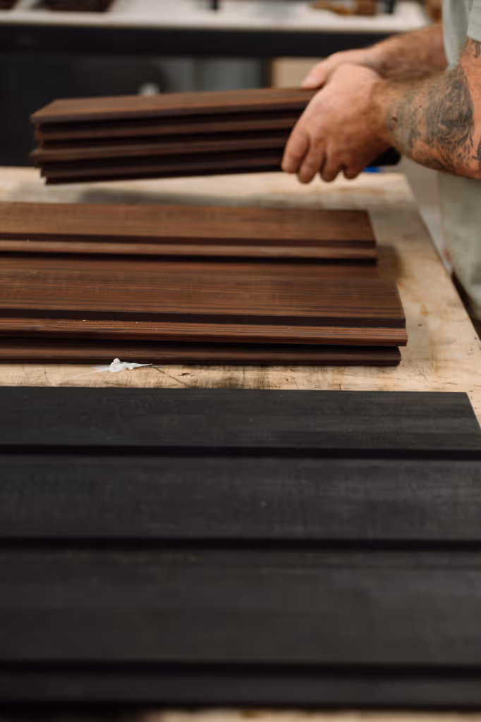 Close-up of a person holding stacked dark wooden planks with other brown and black planks on a workbench being prepared for a Star Bath.