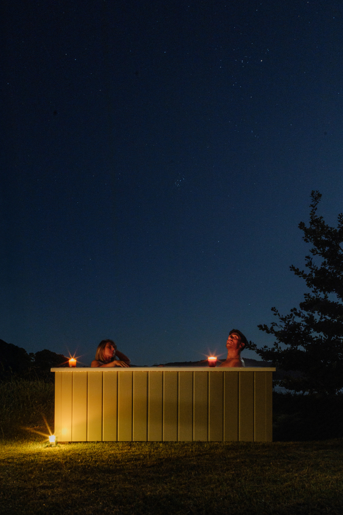 Couple soaking in a Star Bath under a clear starry night sky, with candles glowing.