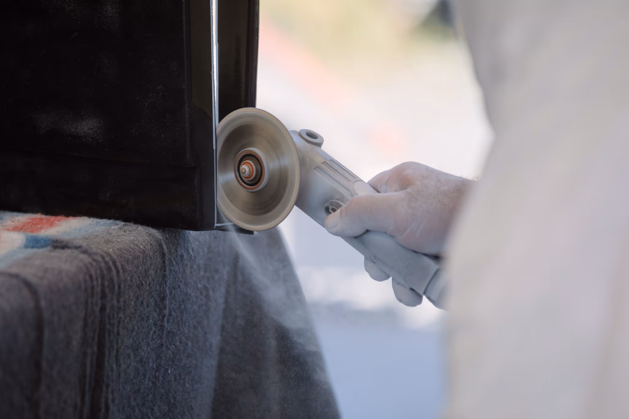Close-up of hand finishing on a Star Bath Fitted Lid using an angle grinder polishing the edge of a black surface with dust particles in the air.