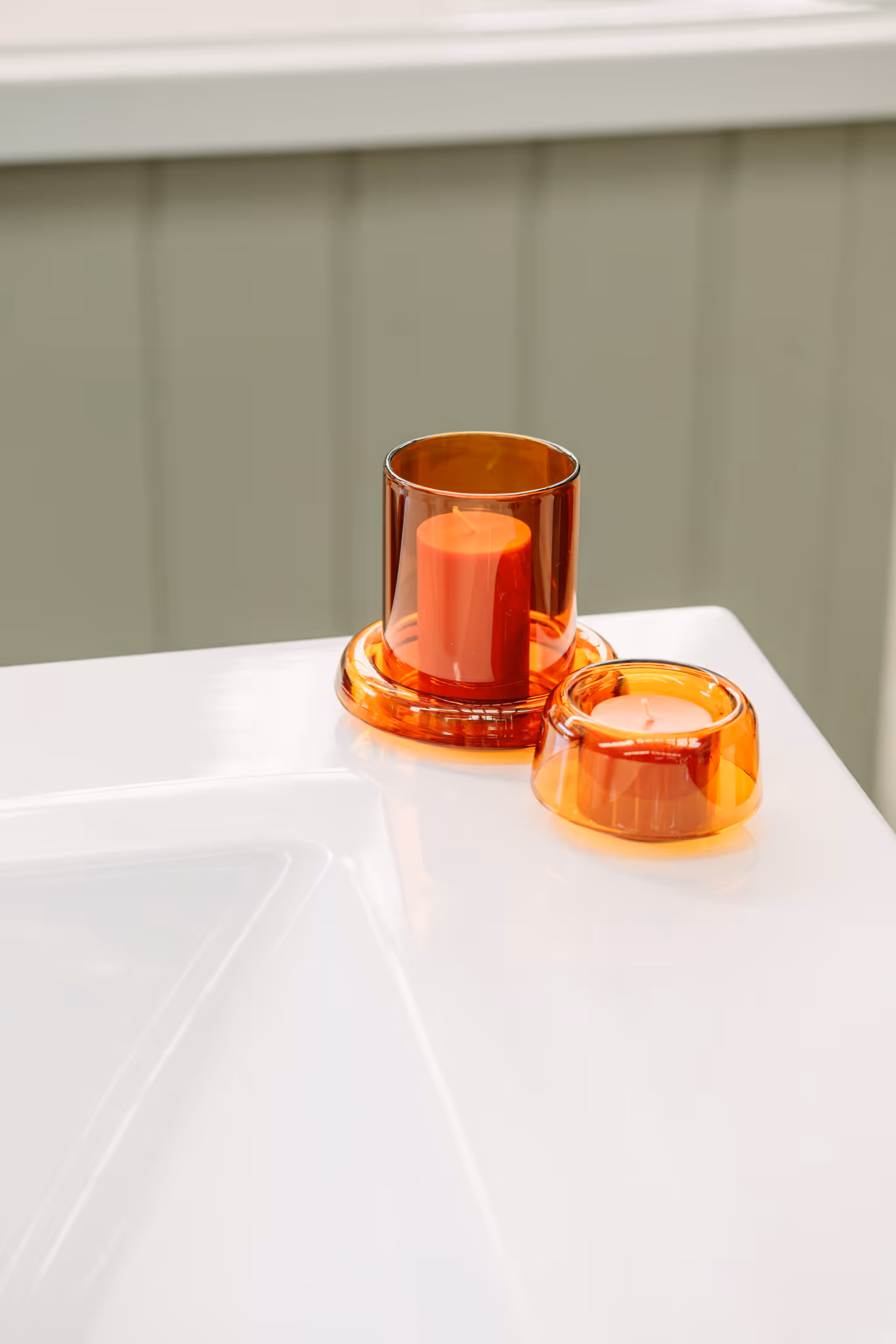 Amber glass candle holders resting on the wide white ledge of a Star Baths outdoor bath in sage painted finish — a generous ledge for beautiful and practical things