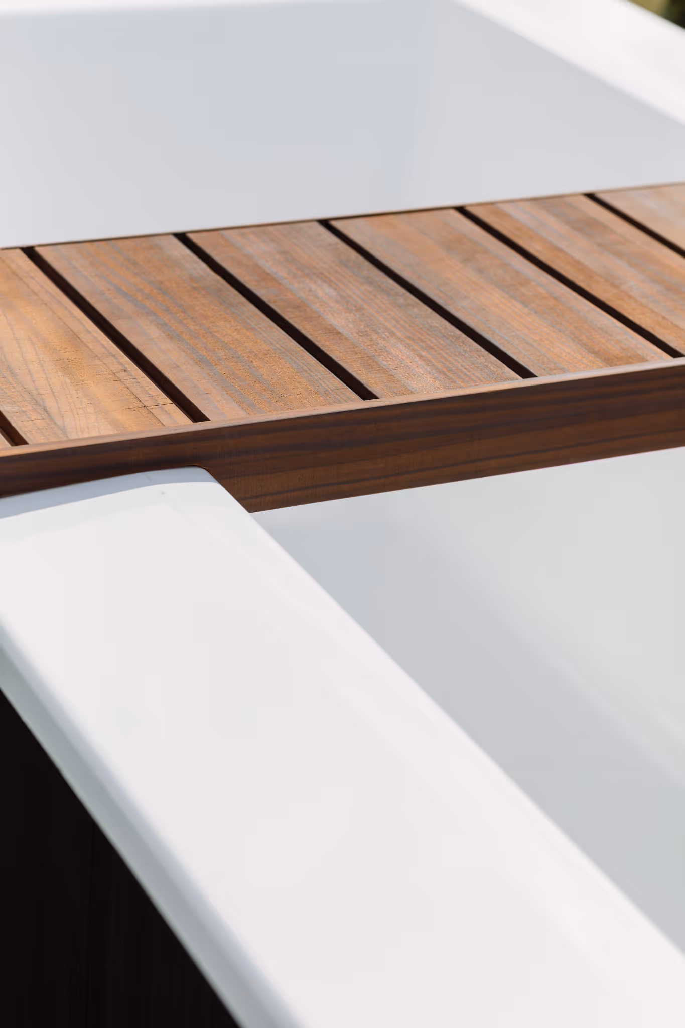 Close-up detail of Star Baths natural teak Retreat Tray resting across a white outdoor bath — beautifully handcrafted timber bath caddy, made in New Zealand