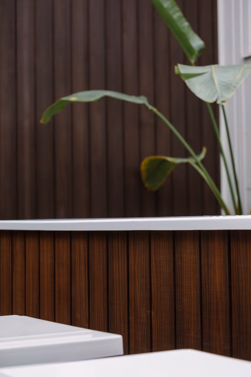Close-up detail of Star Baths outdoor bath clad in beautiful Abodo natural timber with white acrylic surround and tropical foliage