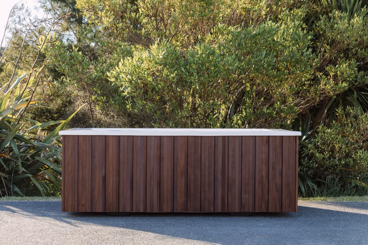 Star Baths Custom Clad outdoor bath with sustainably grown NZ timber in dark walnut stain, native bush backdrop