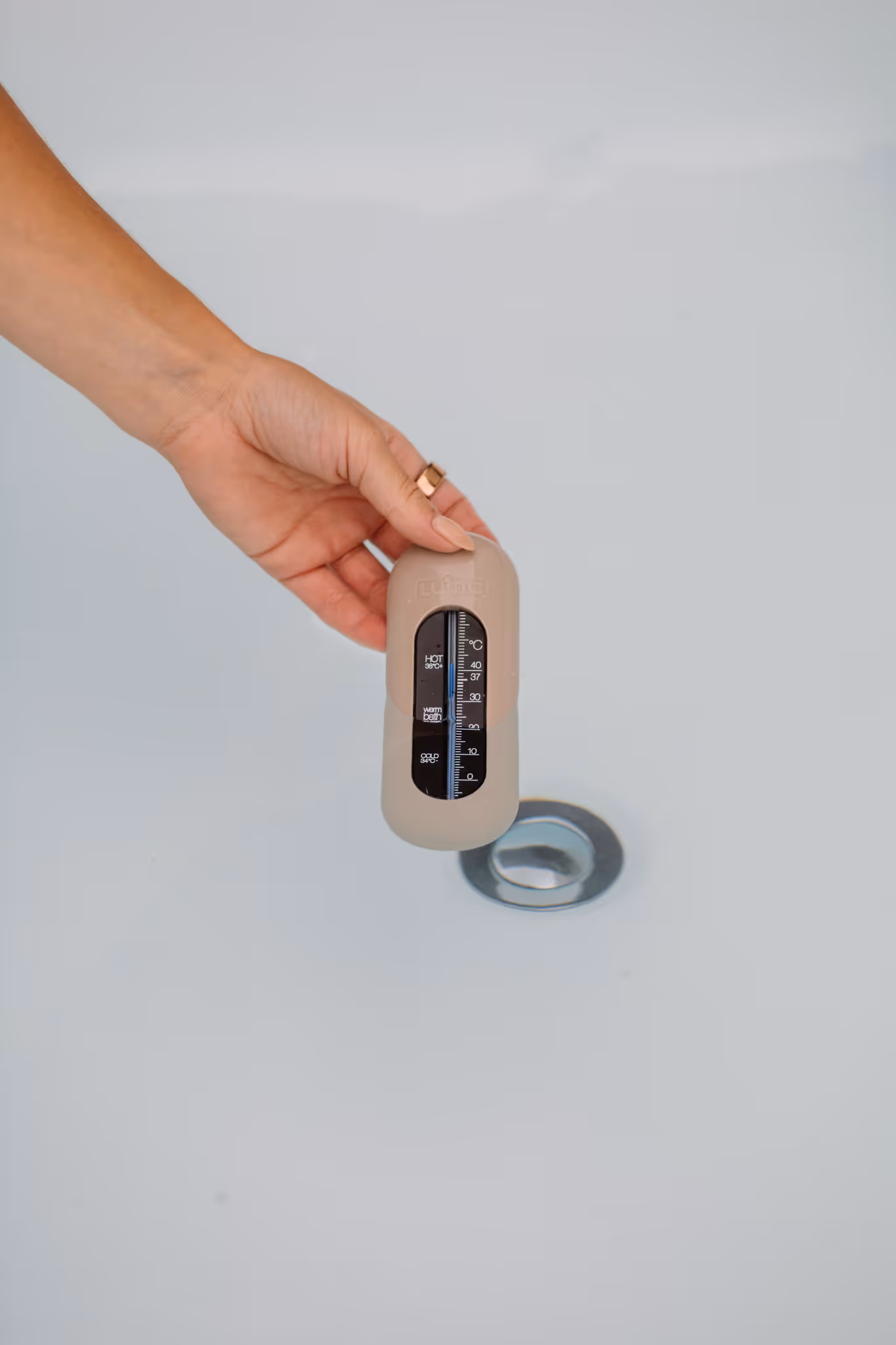 Hand holding a bath thermometer showing hot, warm and cold temperature settings inside a Star Baths fibreglass outdoor bath