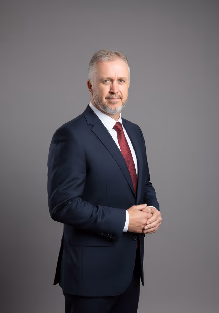 Founder Kevin Morgan in navy suit and red tie standing against a plain gray background.