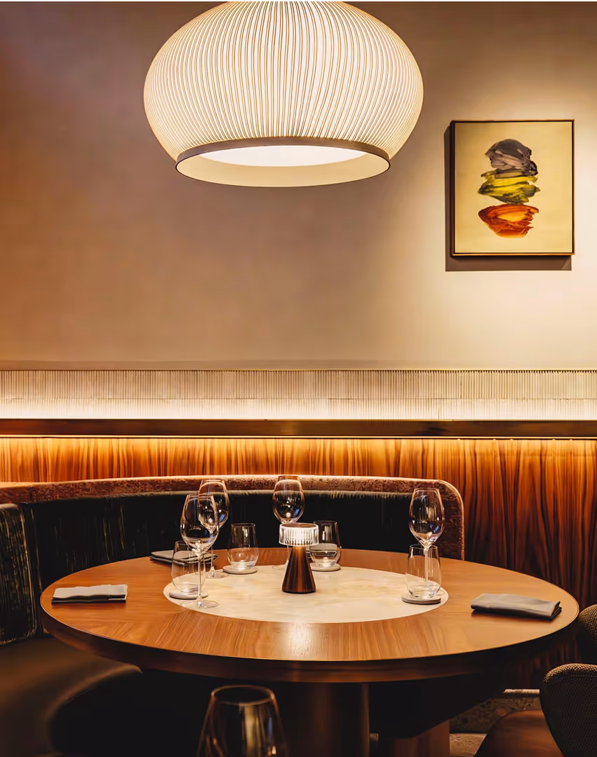 A dining table with booth seating being lit by an overhead pendant light