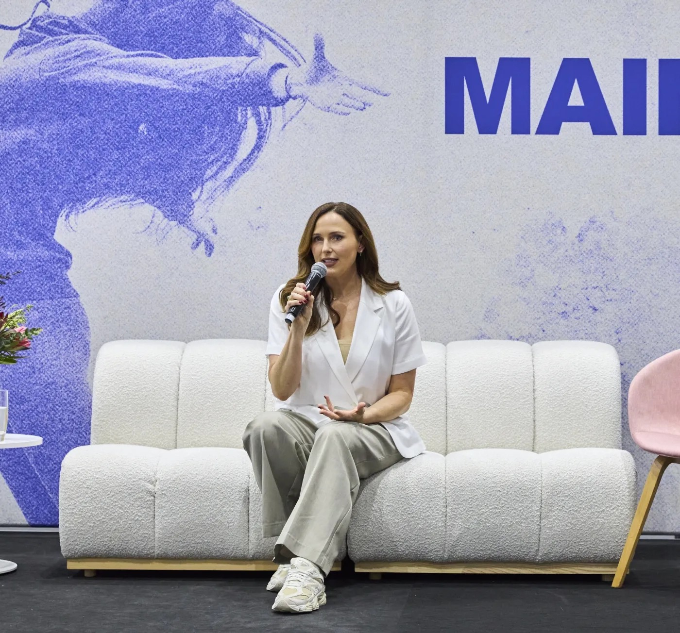 Lucy Quick, founder of The Balanced Elite, engaging in a keynote speech where she sits on a white couch, talking about workplace wellbeing and burnout prevention.