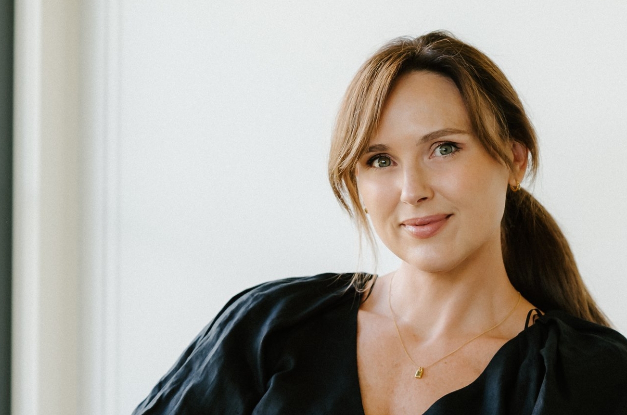 Lucy Quick, founder of The Balanced Elite, subtly and confidently smiling at the camera wearing a black dress.