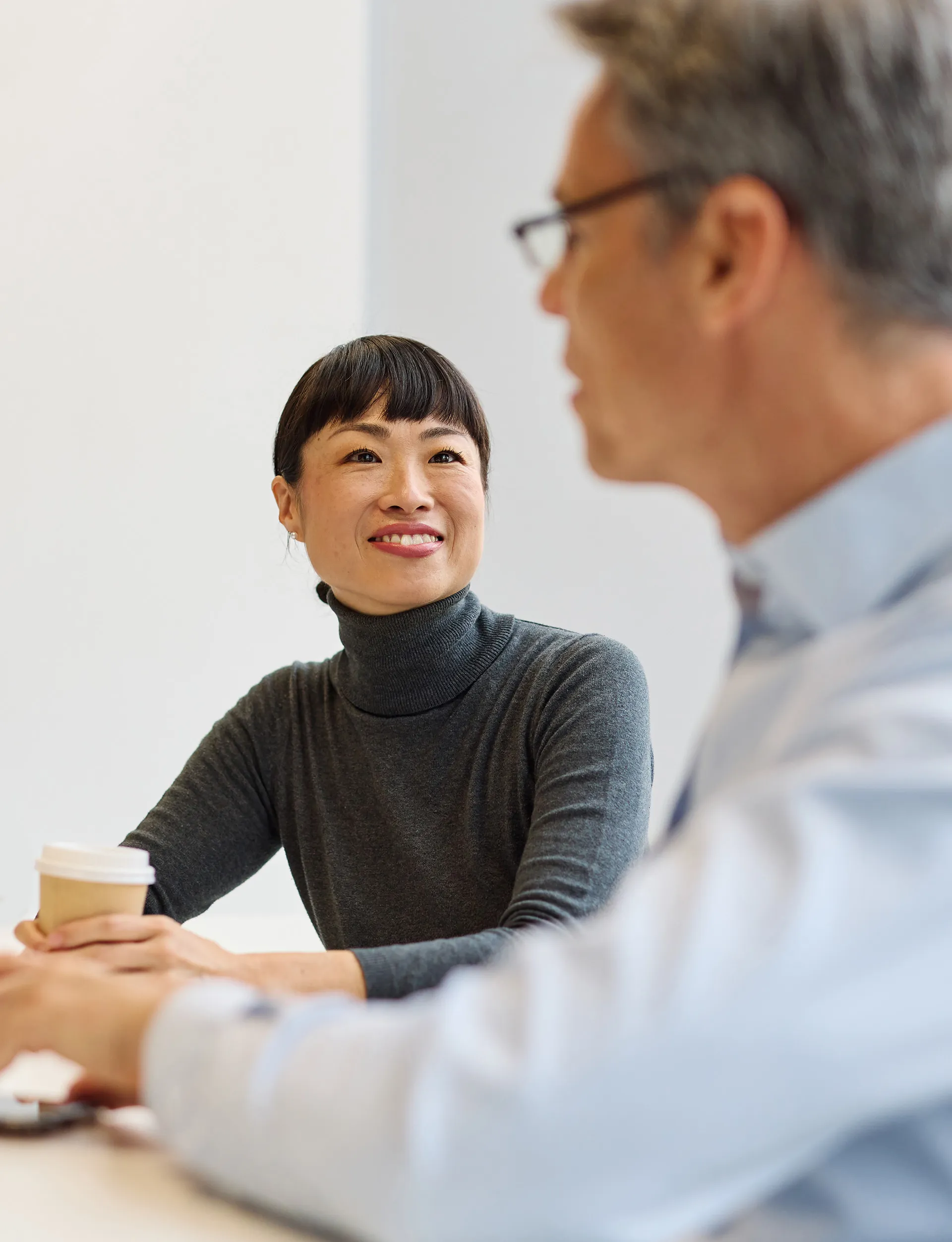 An asian woman looking at a man during a workplace meeting, feeling confident in herself and her ability to lead through the conversation.