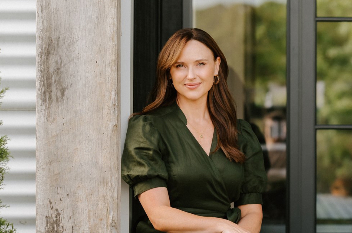 Lucy Quick, founder of the Balanced Elite, looking at the camera in a deep green dress, with reflections in the glass behind her.