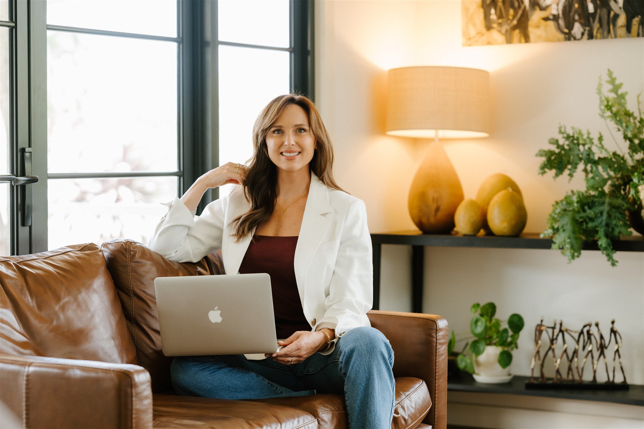 Lucy Quick, founder of the Balanced Elite, sitting comfortably on her couch with a white jacket, working on her workplace wellbeing programs on her laptop.