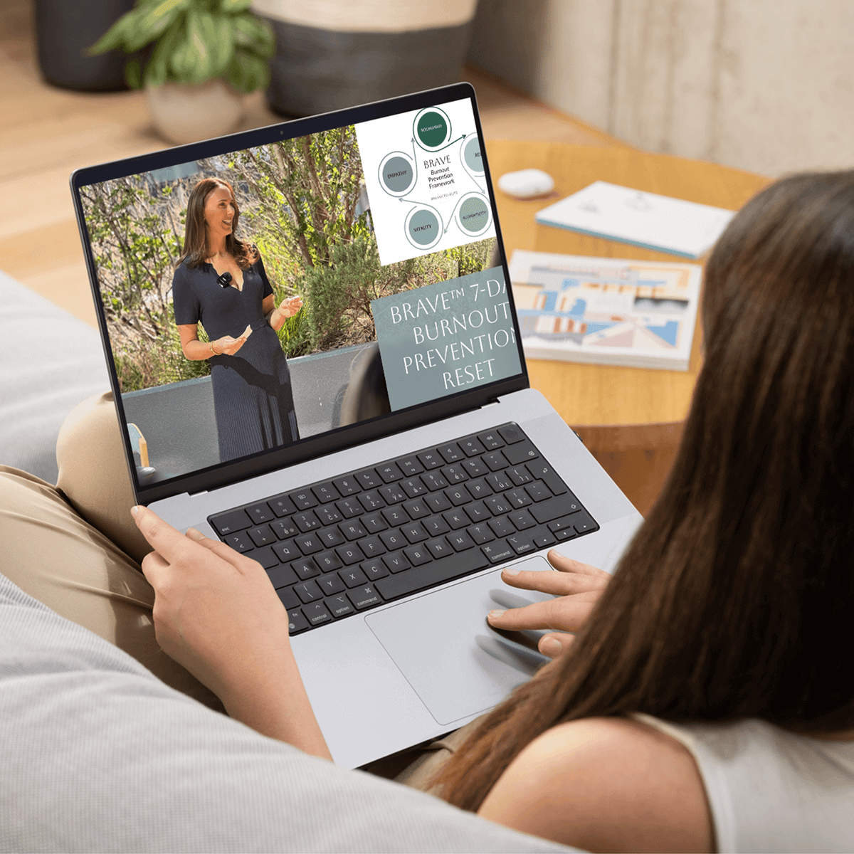 A woman working on her laptop on the couch, watching a video module from the Balanced Elite Burnout Prevention course.