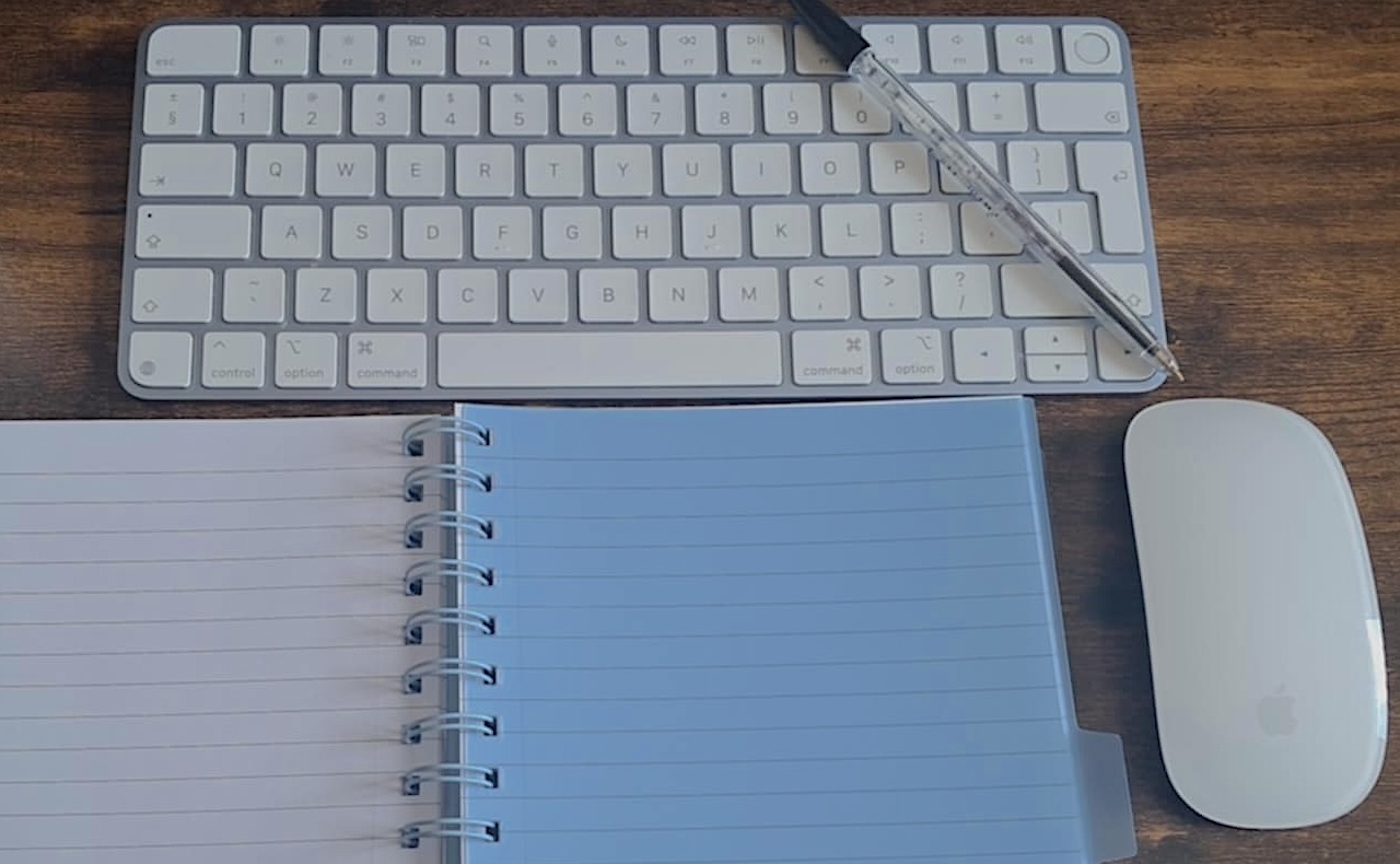 zdjęcie przedstawia klawiaturę, zeszyt, długopis oraz kawałek myszki na biurku z przybliżenia