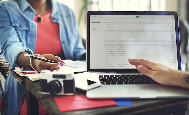 otwarty laptop z położoną rękąna niej, w tle widoczny kawałek kobiety trzymającej ołówek