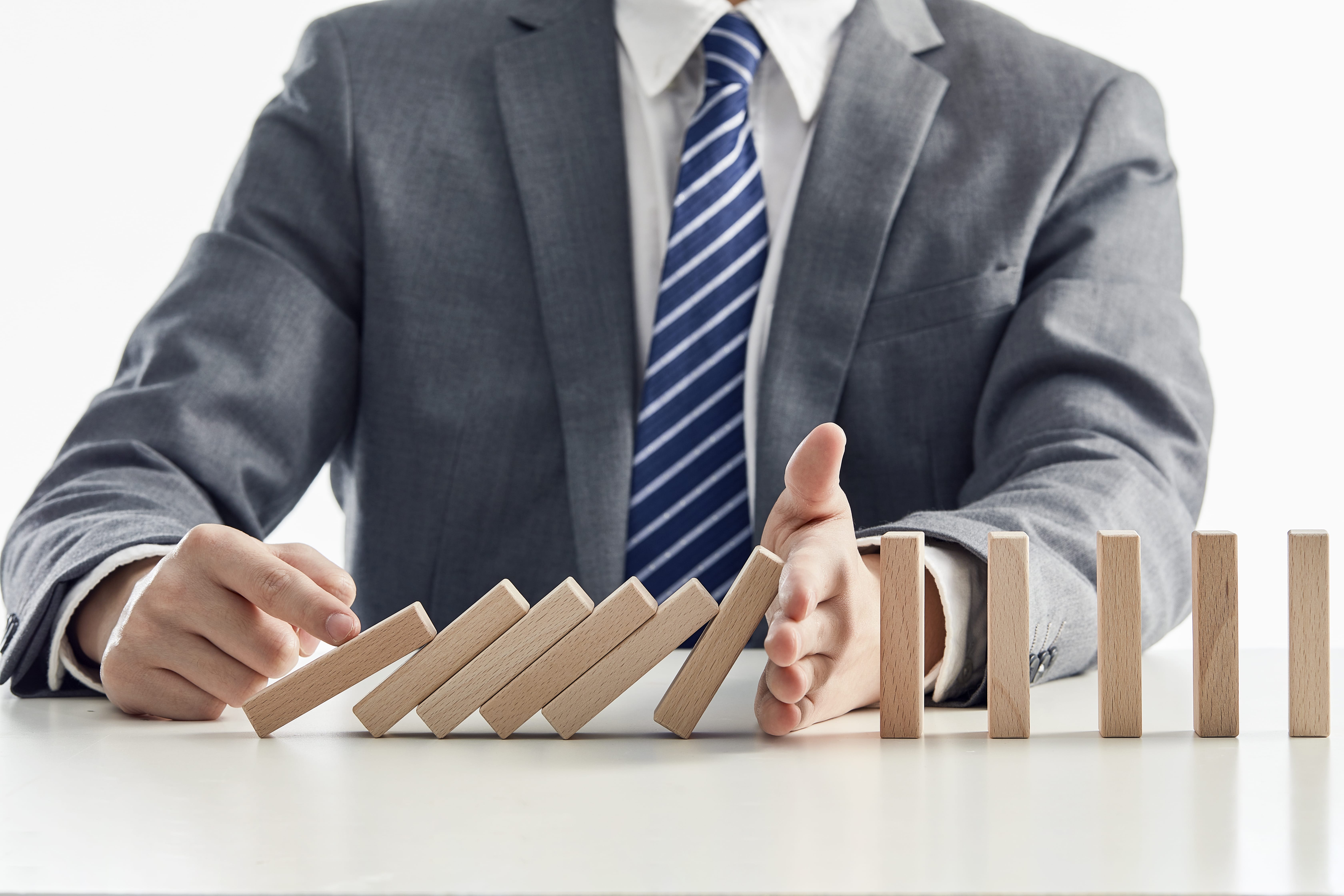 Businessman stops wooden blocks from falling in a domino effect
