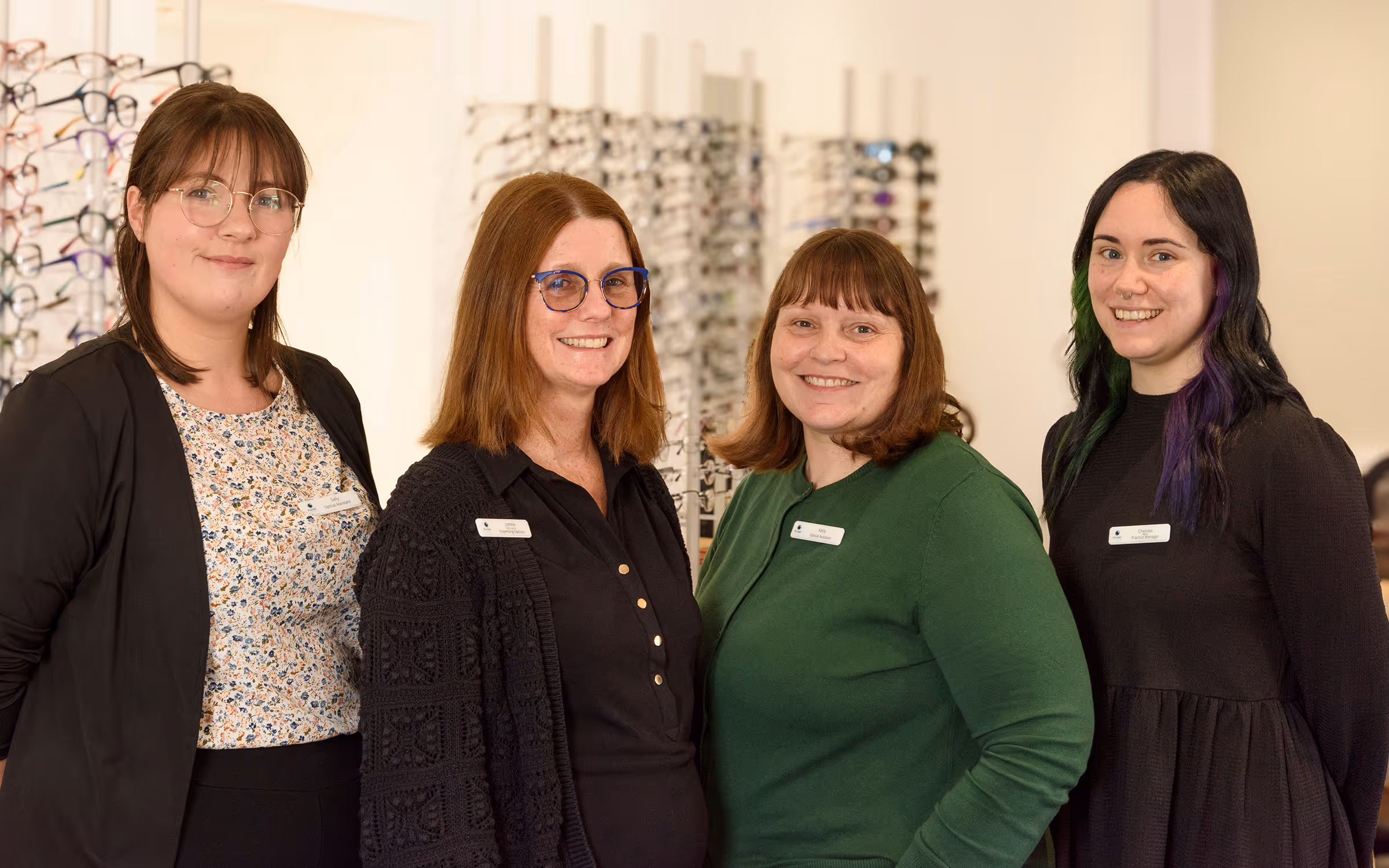 Four smiling optical staff members standing together in eyeglass store