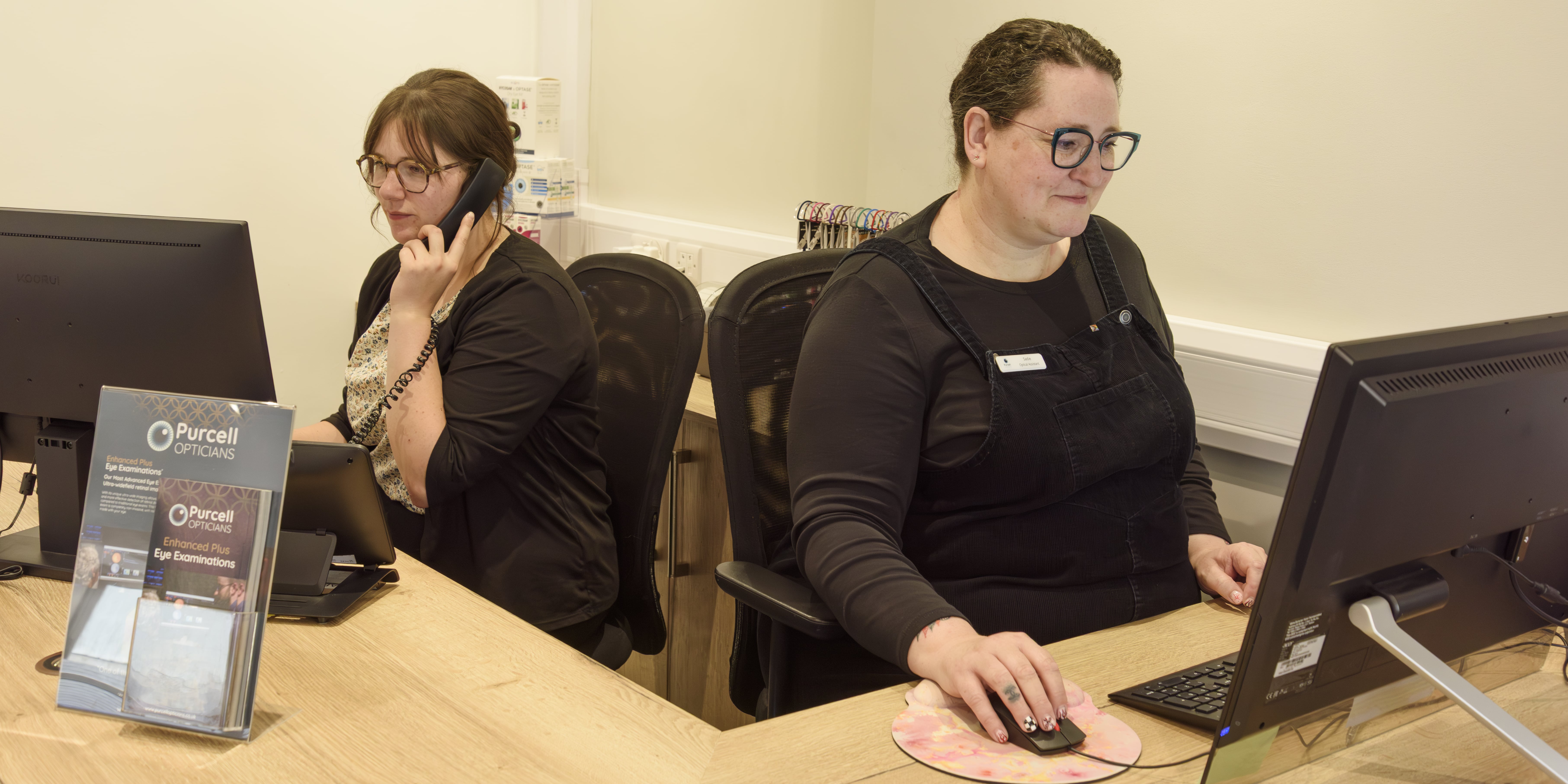 Two opticians working at computers in Purcell Opticians office