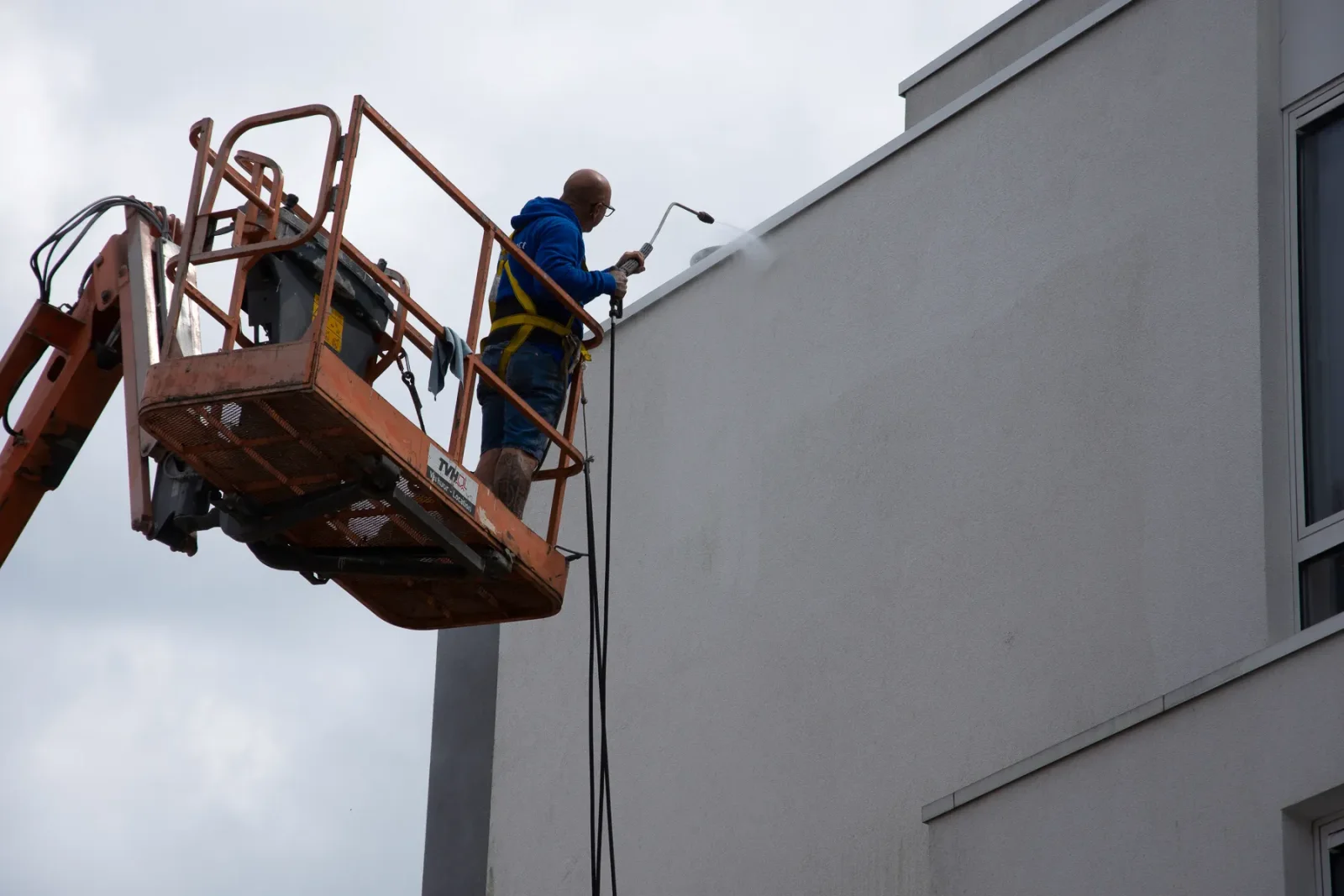 Vakman reinigt hoge crepi-gevel met hogedrukspuit vanuit hoogwerker, als voorbereiding op Energy Protect-behandeling voor langdurige gevelbescherming.