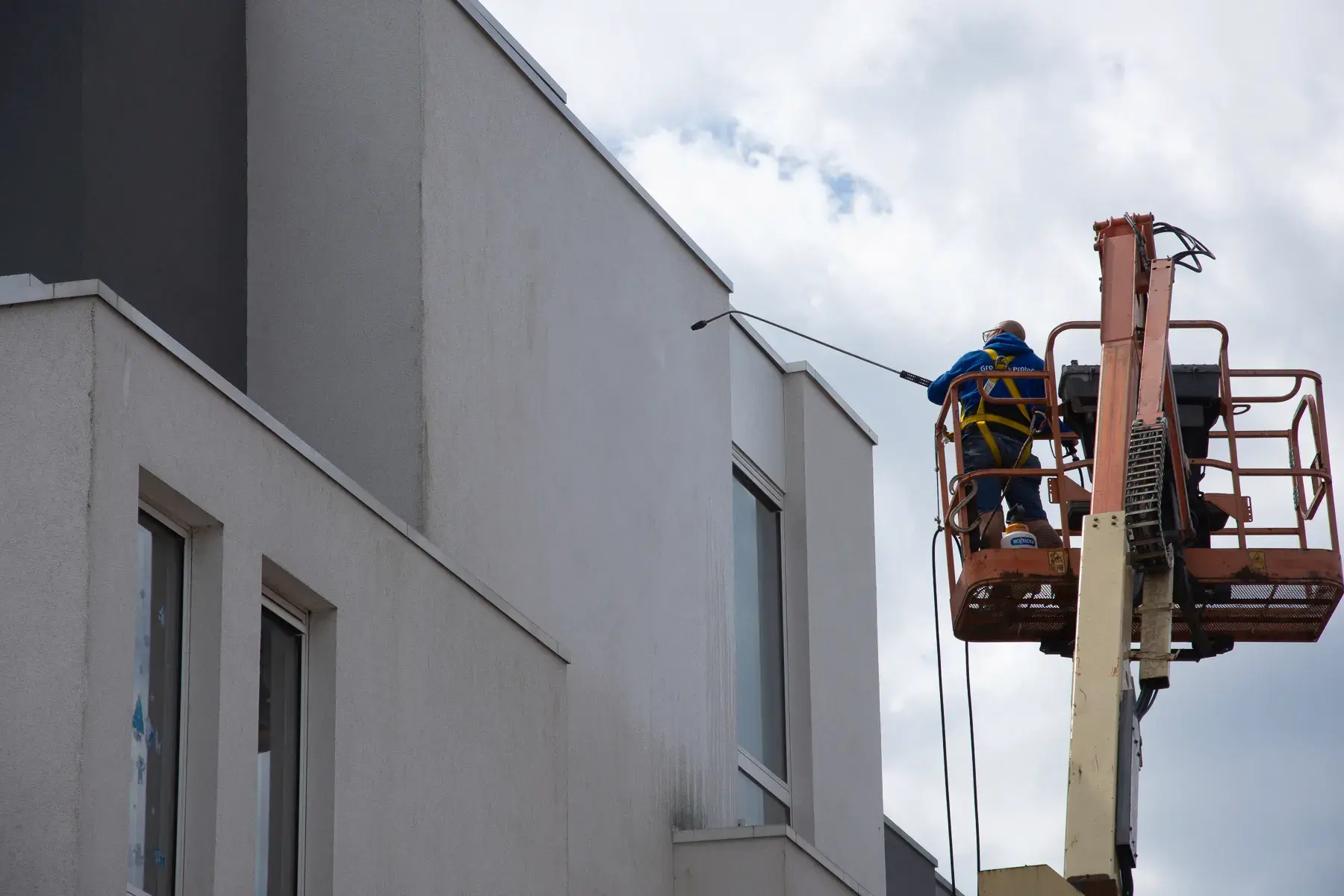 Medewerker reinigt hoge crepi-gevel met hogedrukreiniger vanuit hoogwerker, voorbereid op Energy Protect-behandeling voor duurzame gevelbescherming.