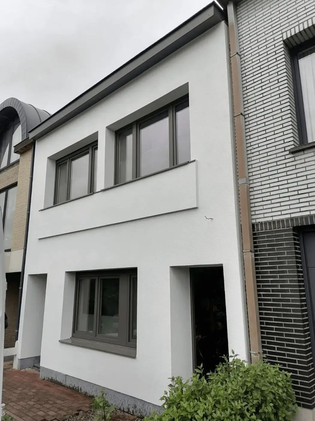 Woning met strakke witte crepi-gevel en grijze kozijnen na gevelrenovatie door Energy Protect voor betere isolatie.