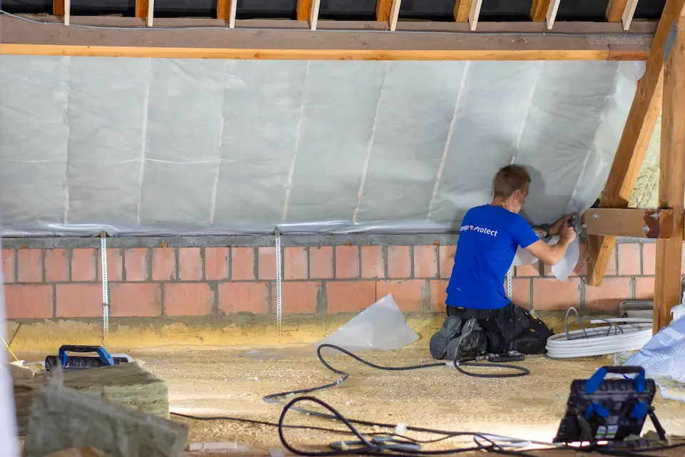 Vakman bevestigt een dampscherm aan een schuin dak voor luchtdichte afwerking en optimale isolatieprestaties.