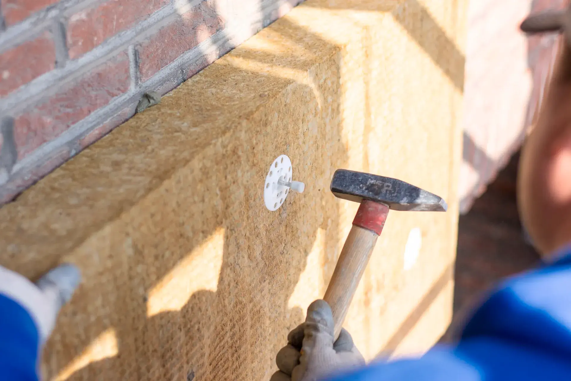 Vakman bevestigt brandwerende isolatieplaat met slagplug tegen buitenmuur van woning, onderdeel van energie-efficiënte renovatie door Energy Protect.